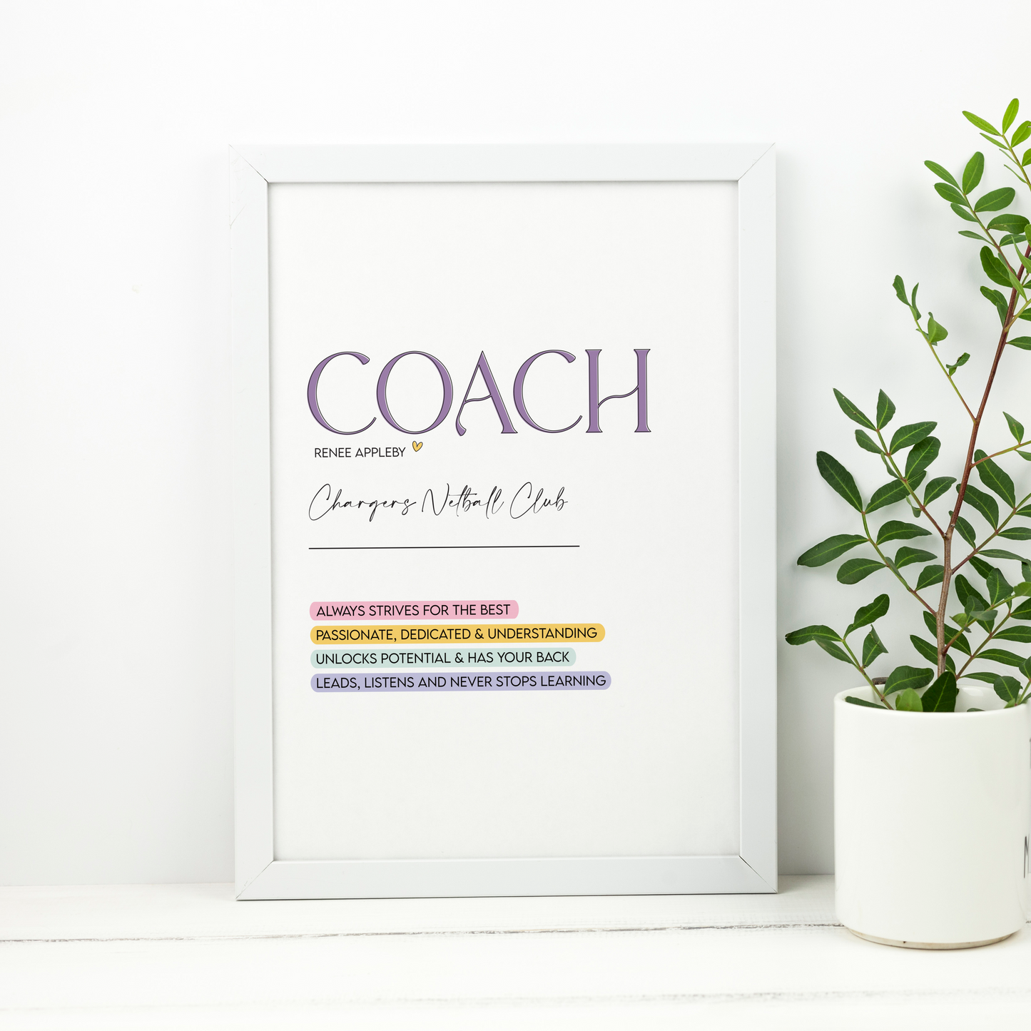 Framed print with motivational text on a white wall next to a potted plant.